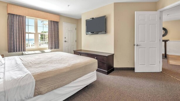 A hotel room with a bed, a dresser, a television, and a door leading to another room.