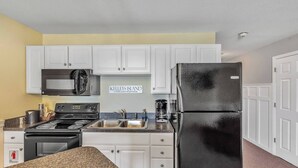 A compact kitchen with white cabinets, a black refrigerator, a microwave, a stove, and a coffee maker.