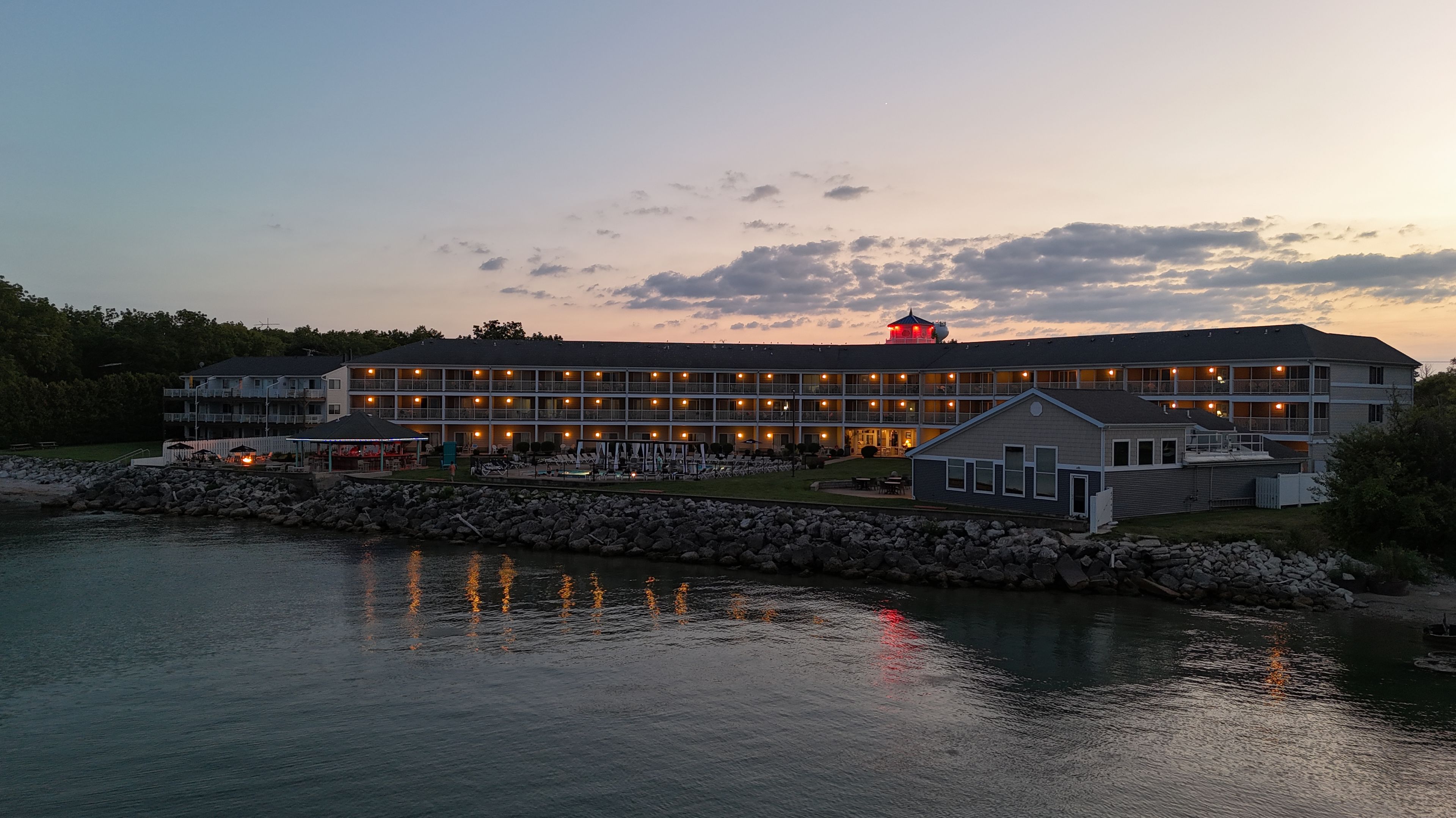 A multi-story hotel with outdoor seating by the water, a covered area, and a distinctive red tower.