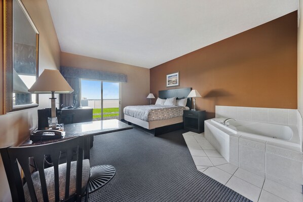 Ein Hotelzimmer mit Bett, Schreibtisch, Stuhl, Lampe, Nachttisch, Badewanne und einem Fenster mit Ausblick.