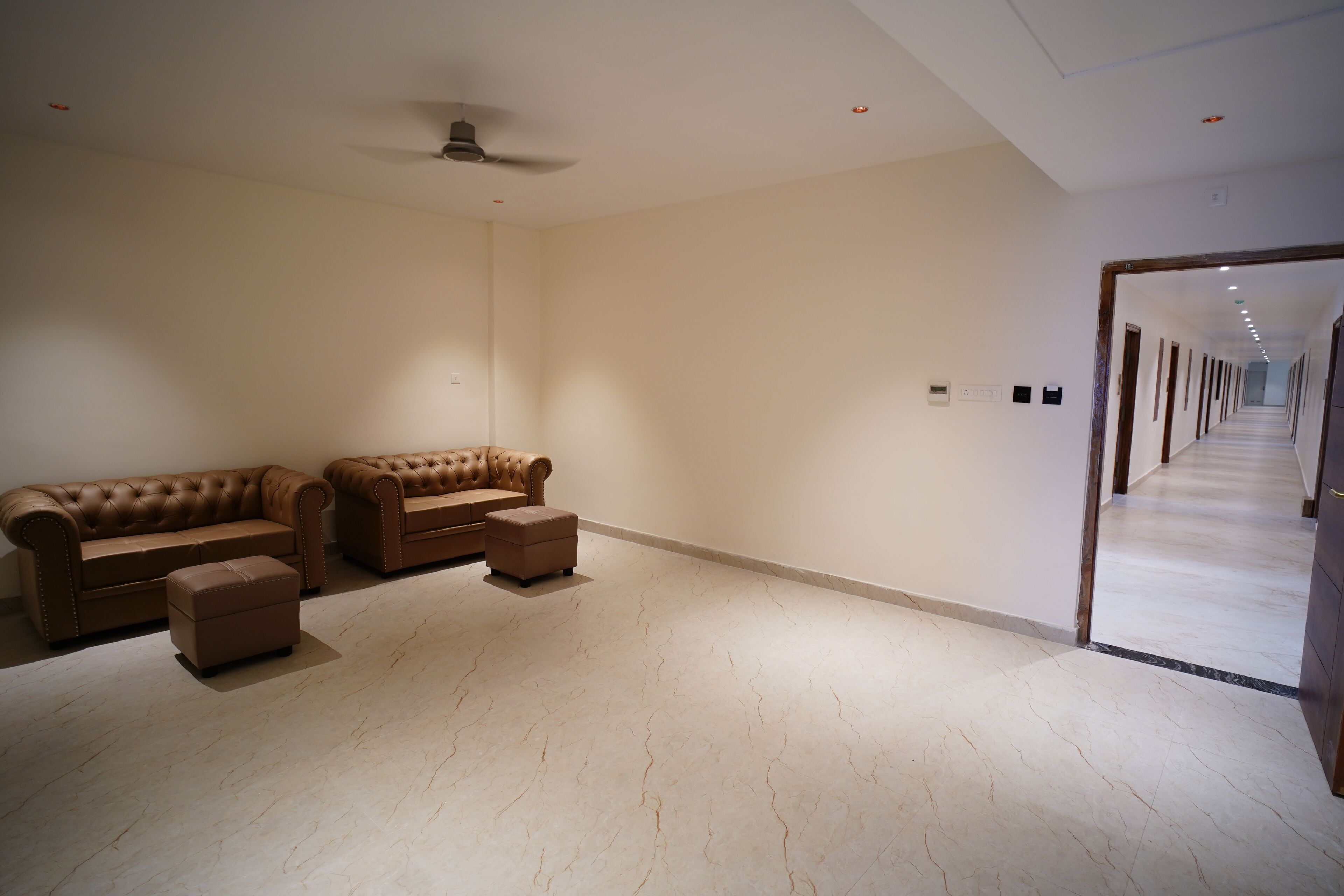 A spacious room with a large beige sofa set, a ceiling fan, and a long hallway leading to another area.