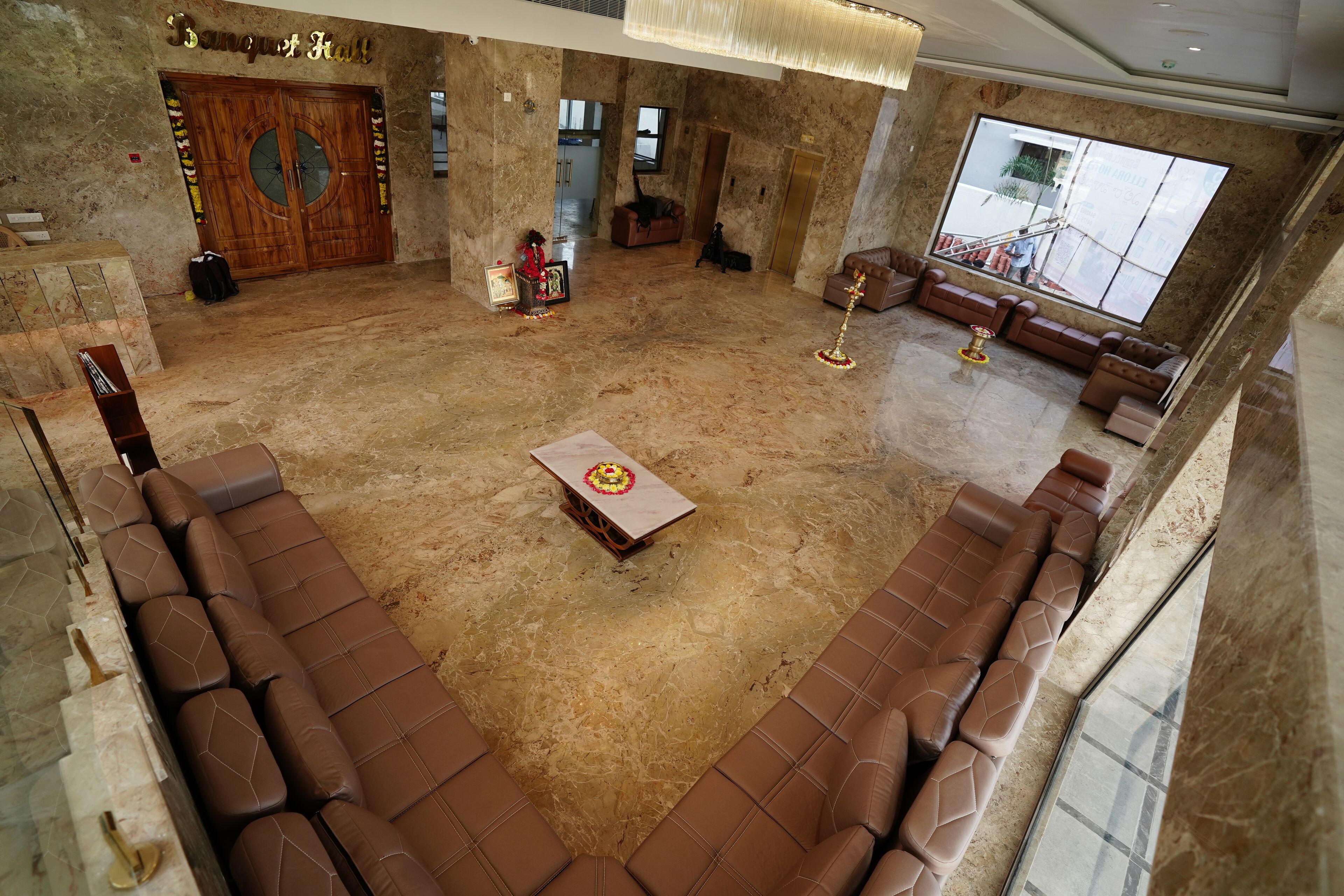 A spacious lobby with a marble floor, a reception desk, a large wooden door, and a seating area with brown leather sofas.