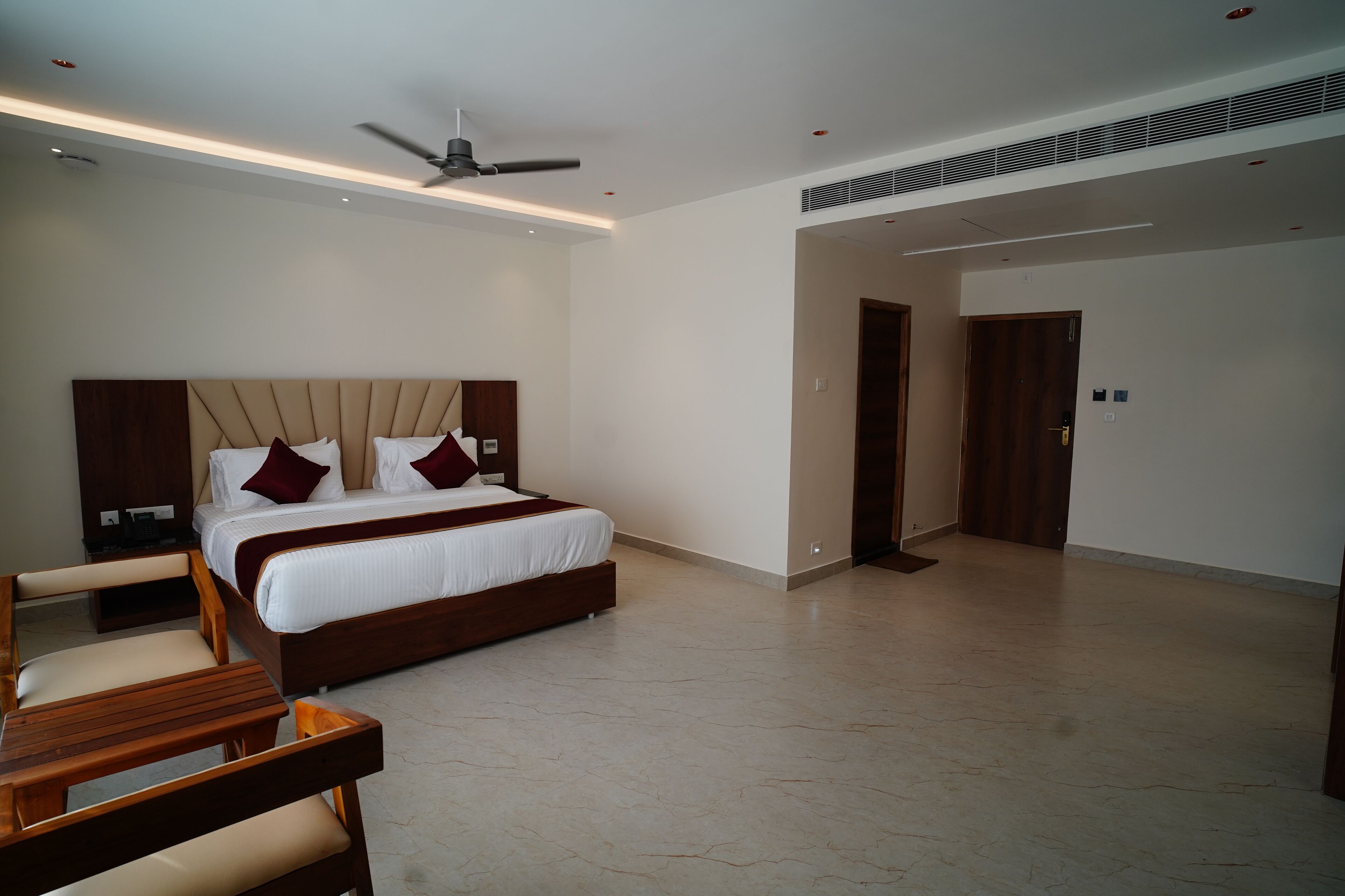 A modern hotel room with a large bed, wooden headboard, and a ceiling fan.