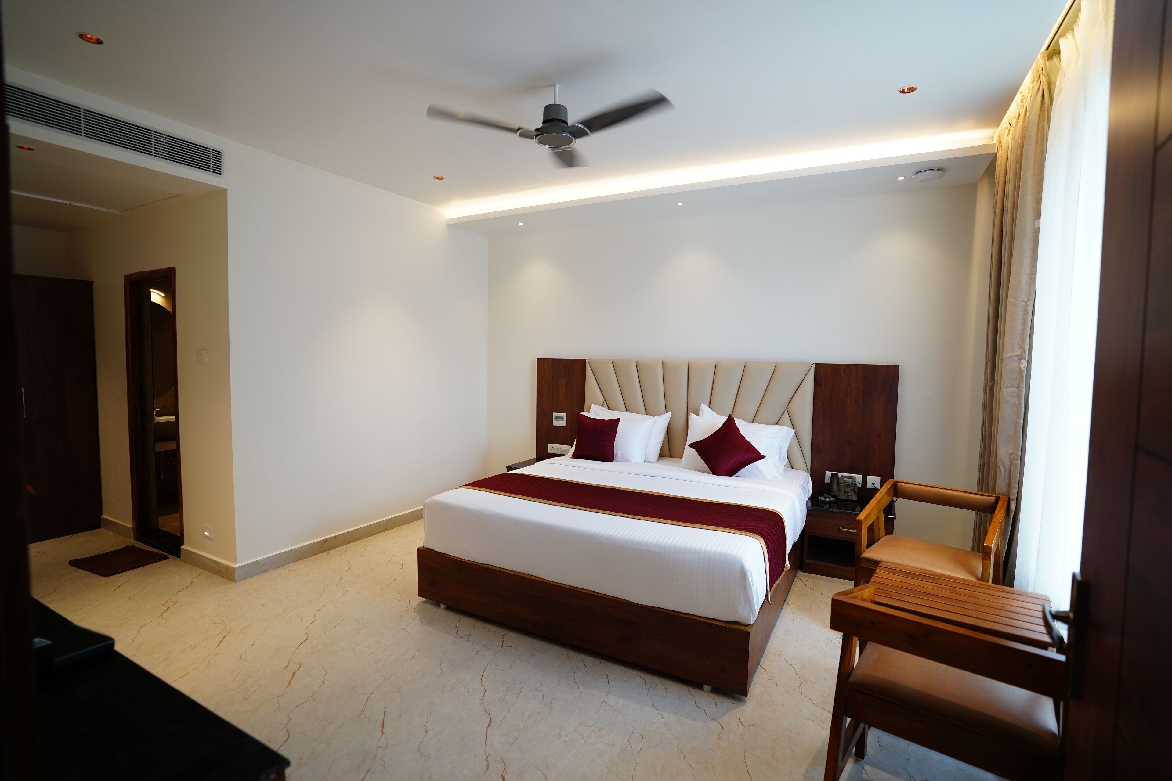 Hotelkamer met een groot bed, een houten nachtkastje, een stoel, een plafondventilator en een deur.
