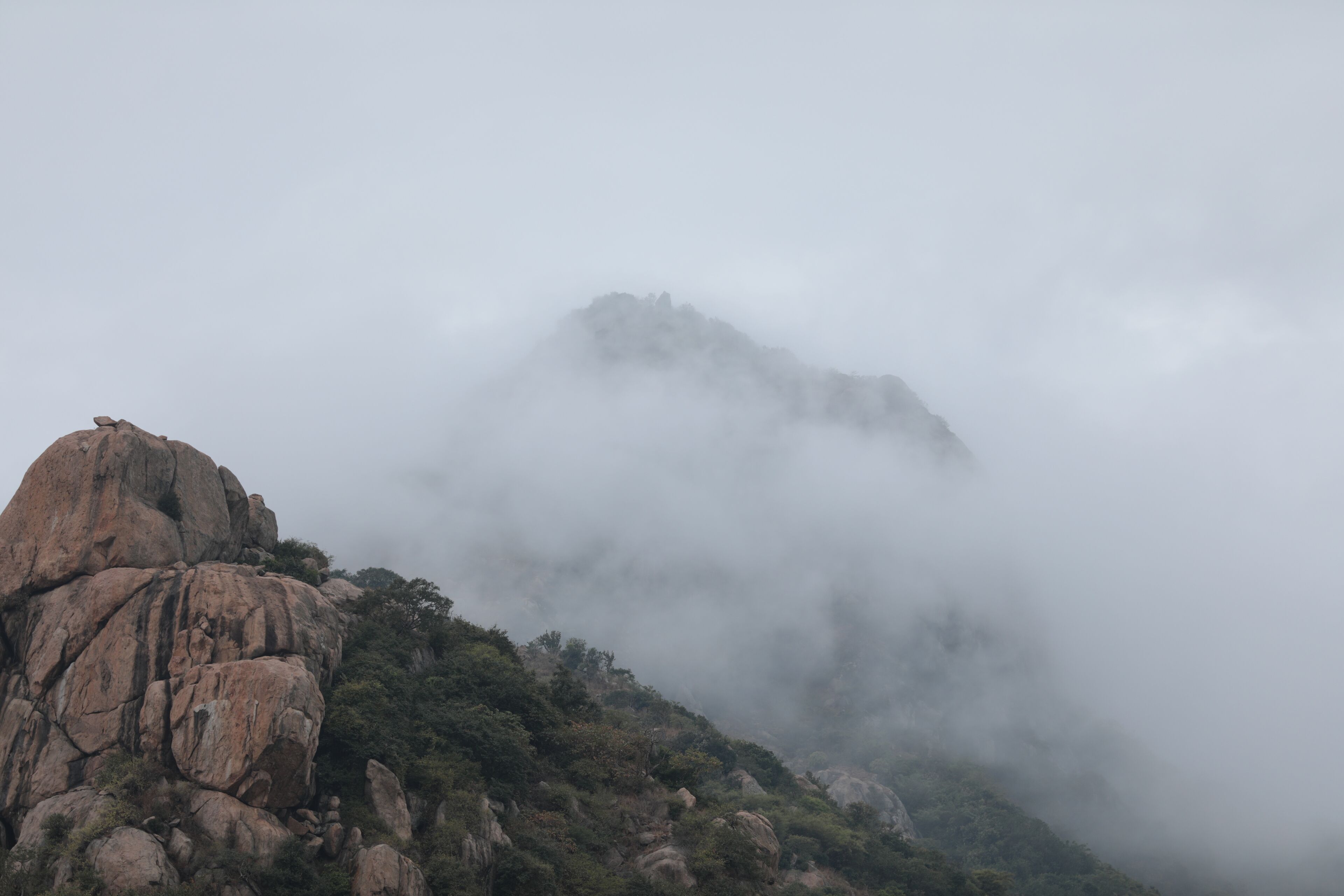 Een bergachtig landschap met een opvallende rotsformatie en dichte mist.