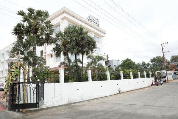 A white building with a black gate, palm trees, and a scooter parked on the street. - Ellora Hotel (Tiruvannamalai)