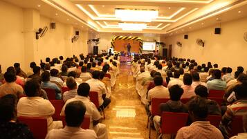 A conference room with rows of chairs facing a stage with a speaker and a presentation screen.