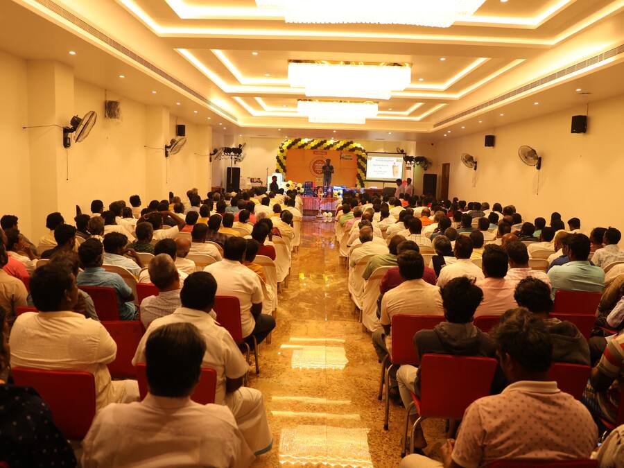A conference room with rows of chairs facing a stage with a speaker and a presentation screen.