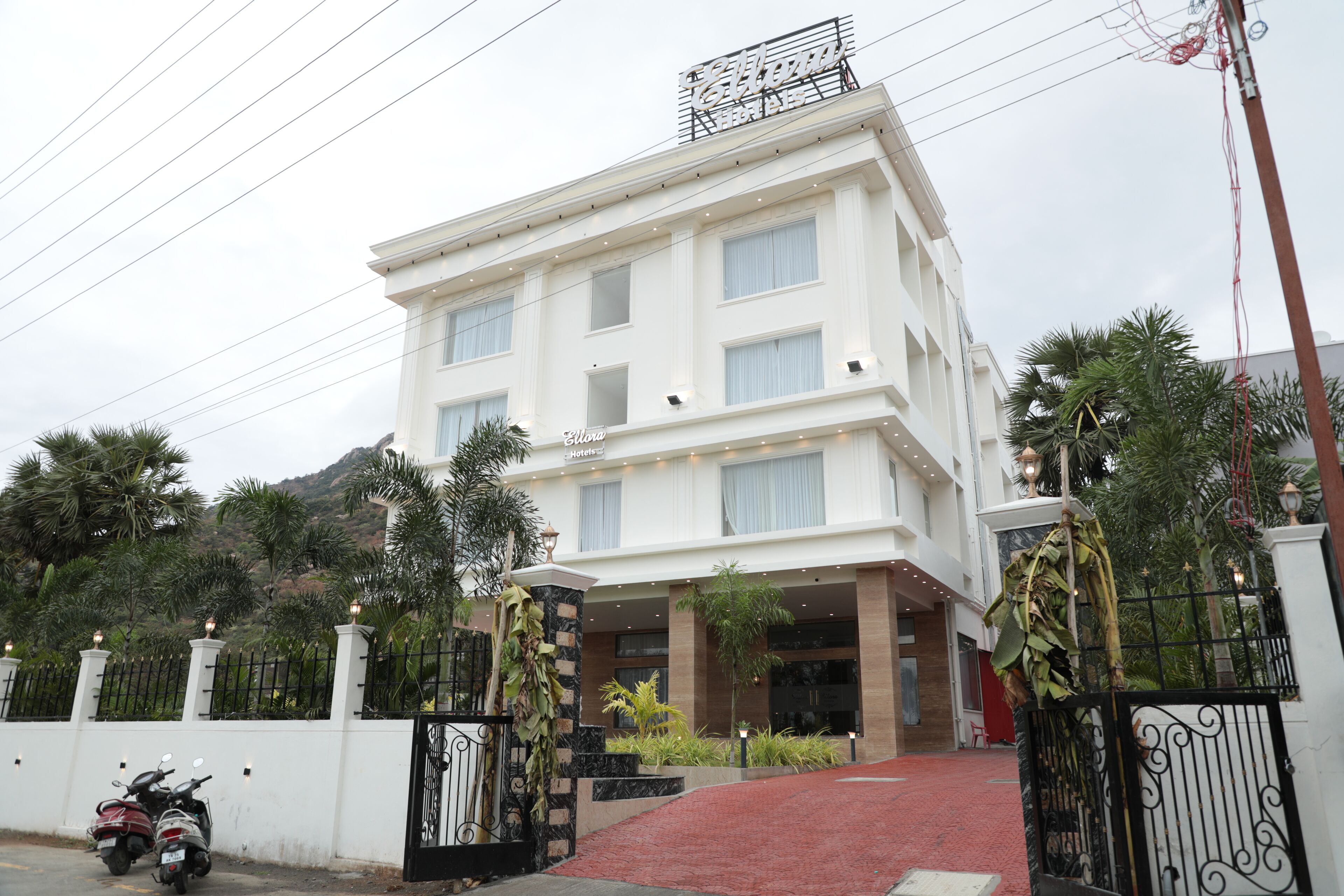 A multi-story hotel with a white facade, a gated entrance, and a red carpet leading to the entrance.