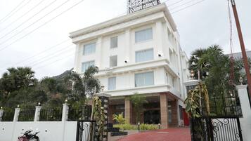 A multi-story hotel with a white facade, a gated entrance, and a red carpet leading to the entrance.
