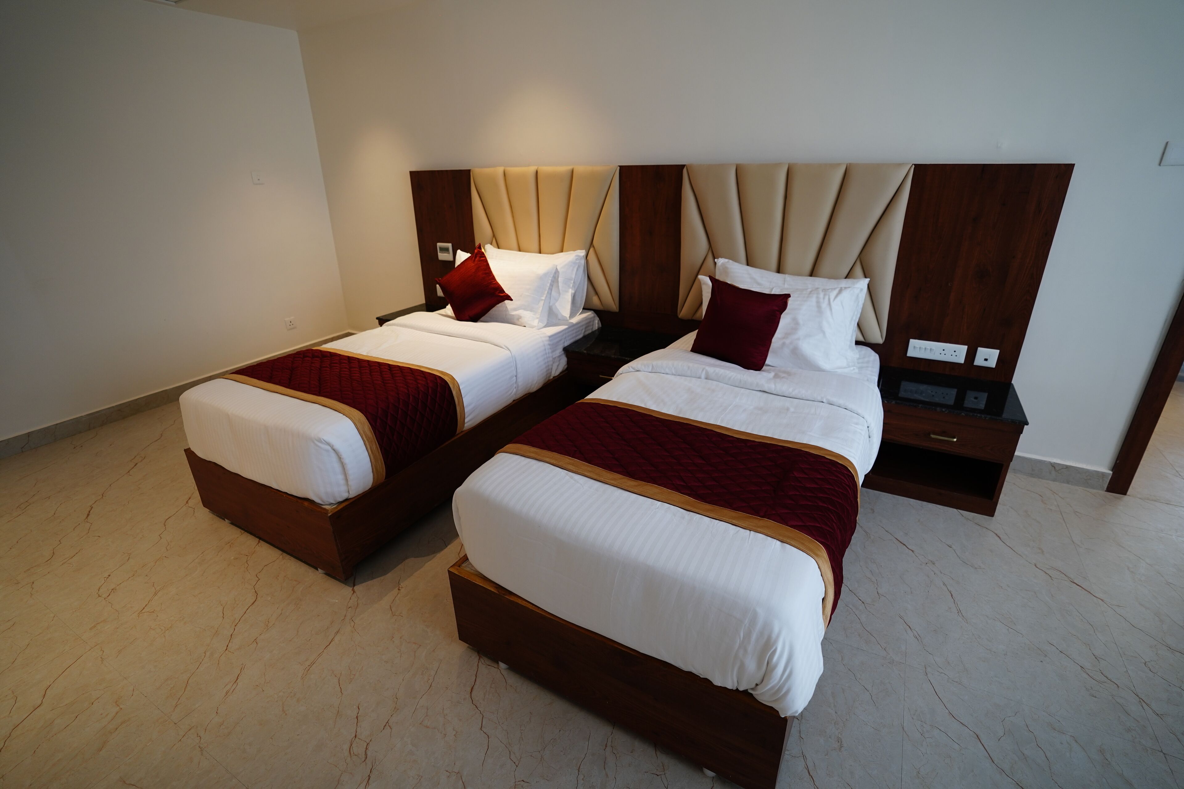 Habitación de hotel con dos camas, cada una con cabecero de madera y ropa de cama blanca.