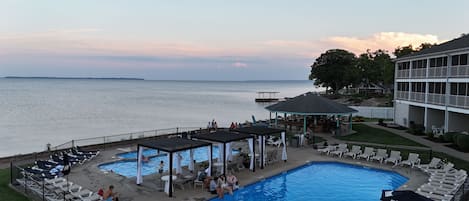 Zona de piscina con sillas de descanso y sombrillas, un bar y vistas al agua.