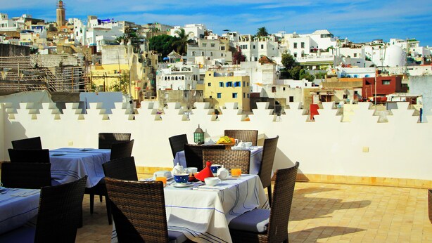 A rooftop dining area with tables and chairs, overlooking a densely packed urban landscape with buildings and a mosque. - dar souran (Tangier)