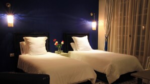 A hotel room with two beds, a nightstand with a vase of flowers, and a window with curtains. - dar souran (Tangier)