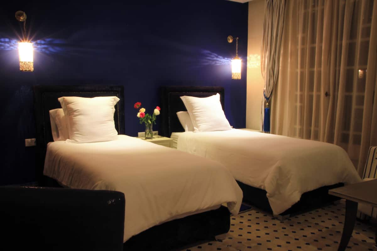 Habitación de hotel con dos camas, una mesita de noche con un florero y una ventana con cortinas.