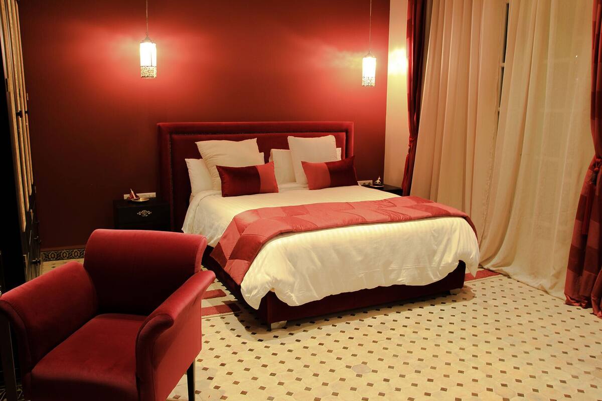 Una habitación de hotel con una cama grande, cortinas rojas y un sillón rojo.