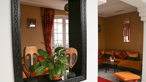 A room with a large mirror reflecting a sofa, a small table, and a potted plant. - dar souran (Tangier)