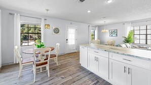 A modern kitchen with white cabinetry, a wooden dining table with chairs, and a large island with a marble countertop. - Beach House~Pet Friendly~Private Pool~Sleeps 14~3min walk to the Beach (Destin)