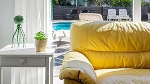 A yellow leather sofa facing a white table with a plant and a decorative item. A pool is visible in the background. - Beach House~Pet Friendly~Private Pool~Sleeps 14~3min walk to the Beach (Destin)