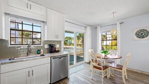 A modern kitchen with white cabinets, a dishwasher, and a dining area with a table and chairs. - Beach House~Pet Friendly~Private Pool~Sleeps 14~3min walk to the Beach (Destin)