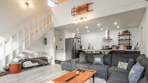 Un salon moderne avec un canapé d’angle gris, une table basse en bois et un escalier menant à un niveau supérieur.