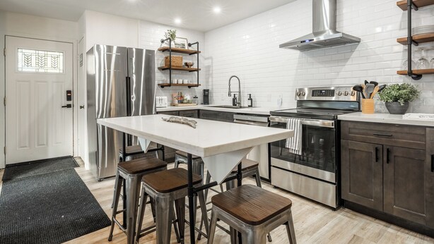 Une cuisine moderne dotée d’appareils électroménagers en acier inoxydable, d’un îlot central avec des tabourets et d’étagères en bois.