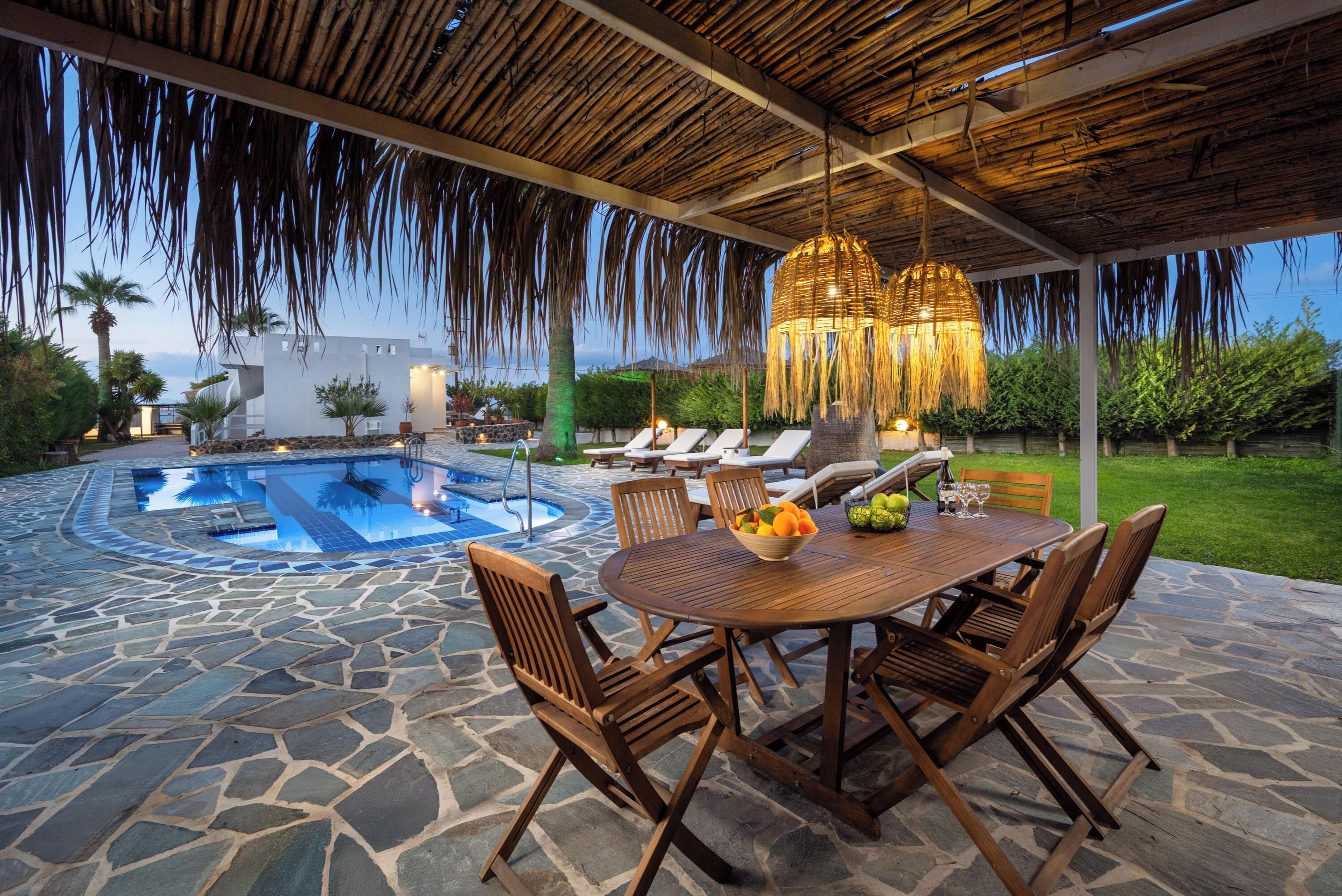 An outdoor pool area with stone flooring, wooden furniture, and a hanging light fixture.