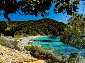 Paisaje costero con aguas turquesas cristalinas, una playa arenosa y una colina boscosa al fondo.