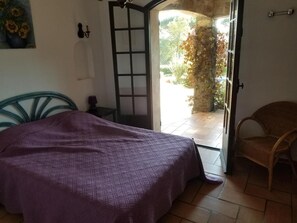 Un dormitorio con cama, una silla, una puerta que da a un espacio exterior y un cuadro en la pared.