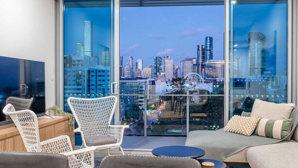 A modern living room with a city view, white wicker chairs, a sofa, and a small round table.