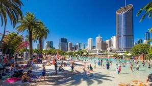 A beach with people, palm trees, and a city skyline in the background.