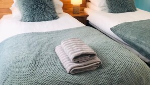 Two twin beds with grey fluffy pillows, a blue abstract painting on the wall, and a bedside lamp. - Cottage - Sleeps 4 - Fireplace - Internet (Penzance)