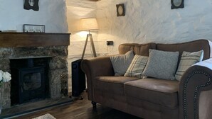 A cozy room with a stone fireplace, a brown leather sofa, and a lamp. - Cottage - Sleeps 4 - Fireplace - Internet (Penzance)