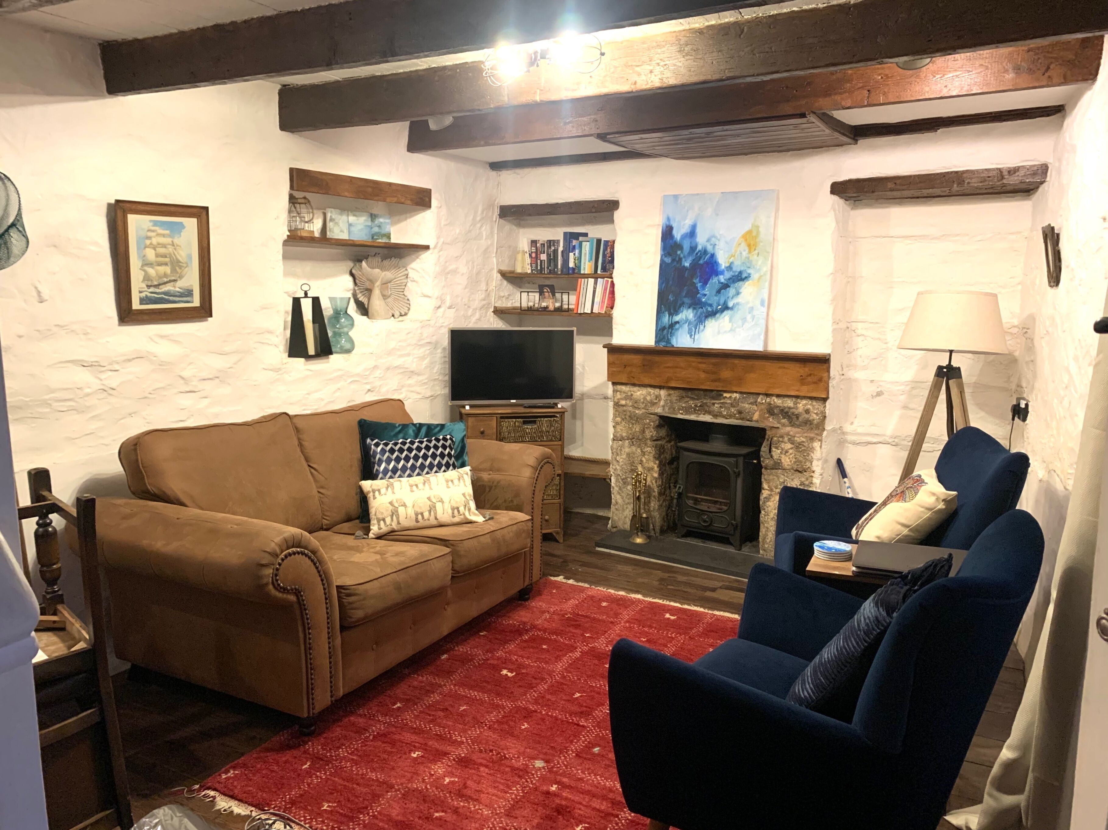 A cozy living room with a brown sofa, a blue armchair, a red rug, a fireplace, and bookshelves.