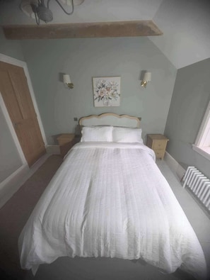 A bedroom with a bed, nightstands, a wall-mounted lamp, and a radiator.
