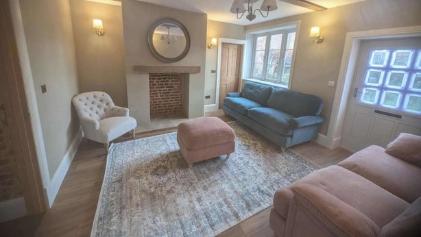 Een woonkamer met een open haard, een witte fauteuil, een blauwe bank en een roze poef.