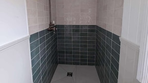 Een kleine douchekamer met betegelde wanden, een douchekop en een toilet.