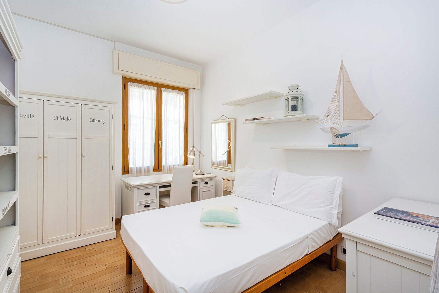 Une chambre à coucher comprenant un lit, un bureau, une chaise, une armoire et une étagère sur laquelle est posé un modèle de voilier.