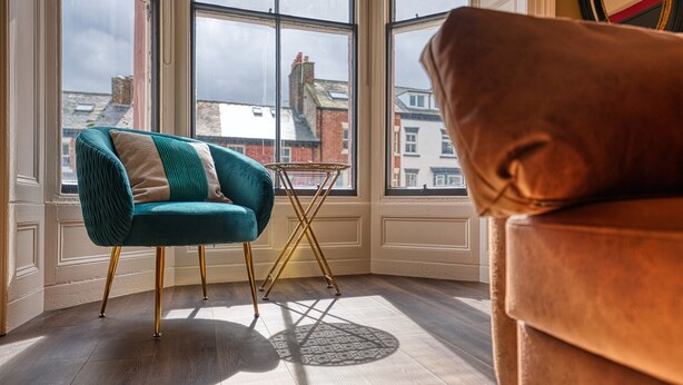 Une pièce avec un fauteuil turquoise, un canapé marron et une petite table surmontée d’un tapis à motifs.