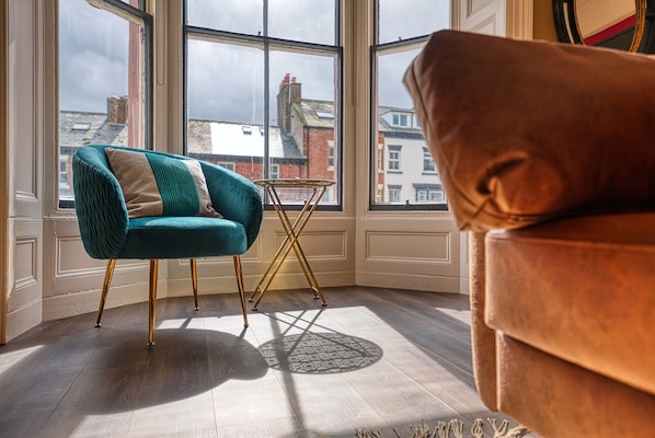 A room with a teal chair, a brown sofa, and a small table with a patterned rug.