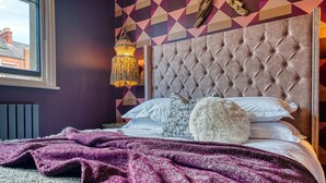 Une chambre à coucher avec une tête de lit capitonnée, un plaid à motifs et un luminaire suspendu.