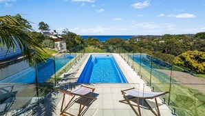 A pool with a clear view of the ocean, surrounded by lush greenery and a house in the background. - Ciao Korora - The Ultimate Coffs Coast Getaway (Korora)