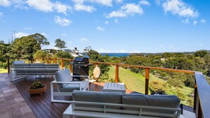 A deck with outdoor furniture, a grill, and a view of the ocean and hills. - Ciao Korora - The Classic (Korora)