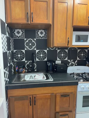 A kitchen with wooden cabinets, a black countertop, a stainless steel sink, a microwave, a gas stove, and patterned tiles.