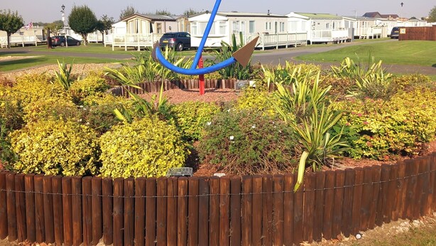 A park with a blue sculpture, a wooden fence, and a row of mobile homes in the background. - 3bed-sleeps6-pet Friendly-familyfriendly (Mablethorpe)