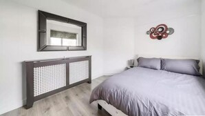 A bedroom with a bed, a dresser, a mirror, and a wall decoration. - 2br-sleeps6-parking-garden-nearlondon (Sunbury on Thames)