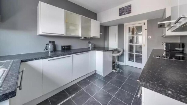 A modern kitchen with white cabinets, a black countertop, and a tiled floor. - 2br-sleeps6-parking-garden-nearlondon (Sunbury on Thames)