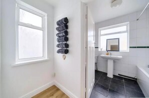 A bathroom with a white sink, a mirror, and a towel rack with multiple towels. - 2br-sleeps6-parking-garden-nearlondon (Sunbury on Thames)