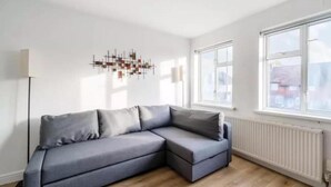 A modern living room with a grey sectional sofa, a floor lamp, and a contemporary art piece on the wall. - 2br-sleeps6-parking-garden-nearlondon (Sunbury on Thames)