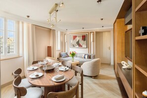 A modern dining area with a wooden table set for four, a grey sofa, and a bookshelf with a cross-shaped decoration. - Merveil - Signature Suite - Louvre - Bourse II (Paris)